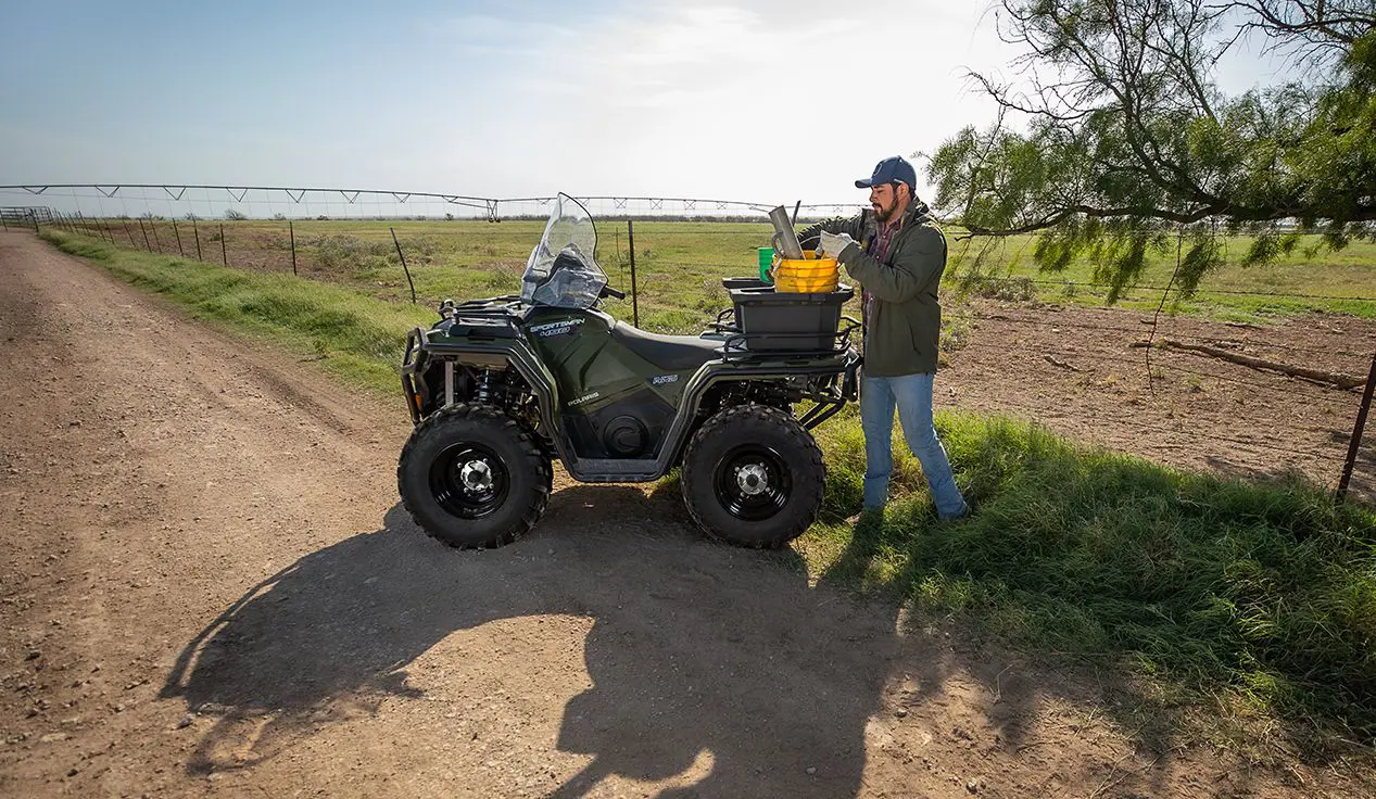 Farmer using the cargo rack on a Polaris Sportsman 450 ATV to haul fencing materials.
