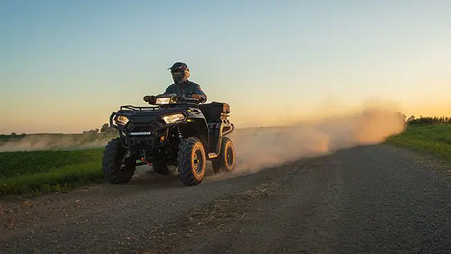 Polaris Sportsman 450 ATV driving down a dirt road.