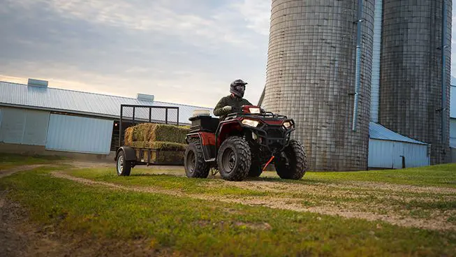 Polaris Sportsman 450 ATV pulling a trailer full of square bales.