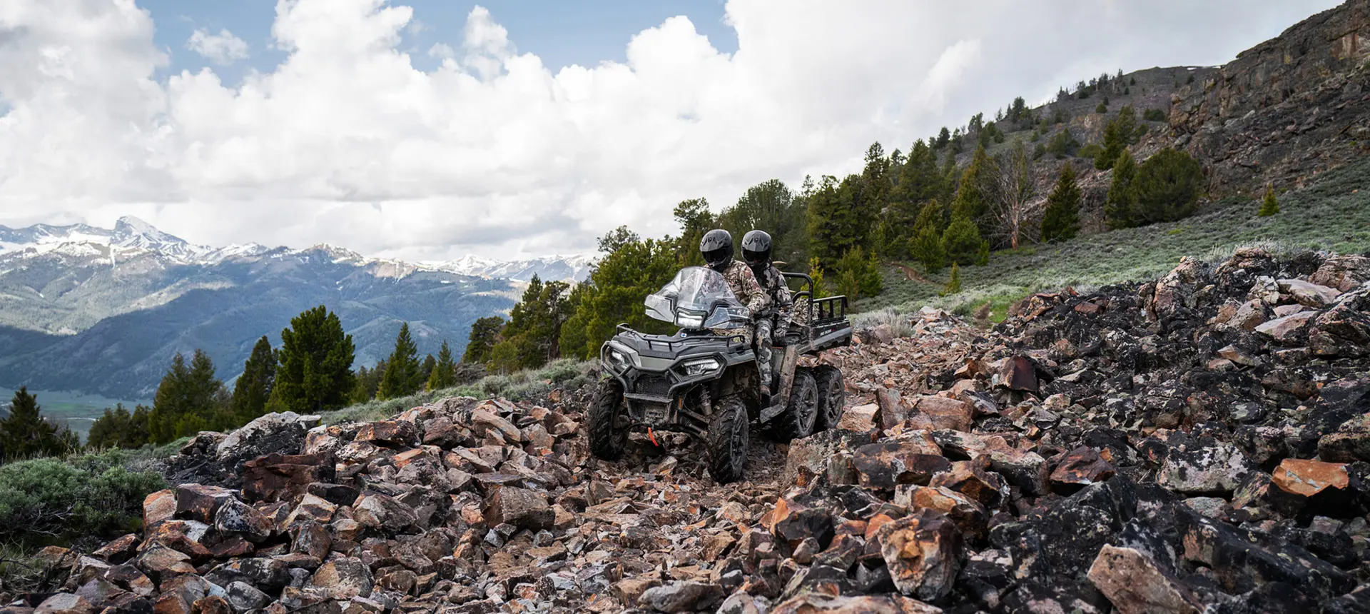 Two hunters riding over rocky terrain on a Polaris Sportsman 6x6 570 ATV.