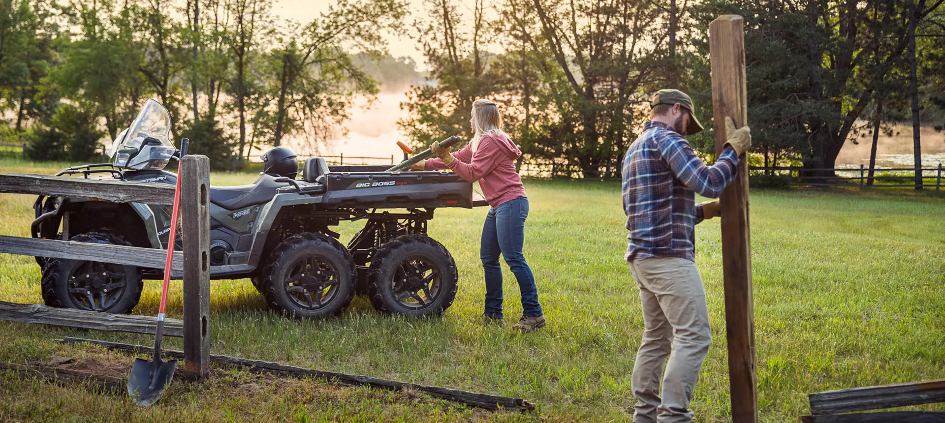 2 people using the cargo box on their Polaris Sportsman 6x6 570 ATV to haul fence posts.