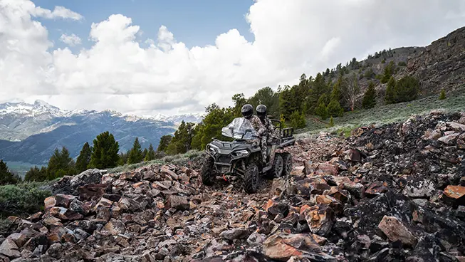 Two hunters riding over rocky terrain on a Polaris Sportsman 6x6 570 ATV.