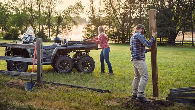 2 people using the cargo box on their Polaris Sportsman 6x6 570 ATV to haul fence posts.