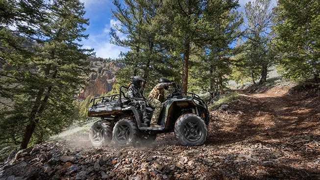 Side profile of a two people riding a trail on a Polaris Sportsman 6x6 570 ATV.