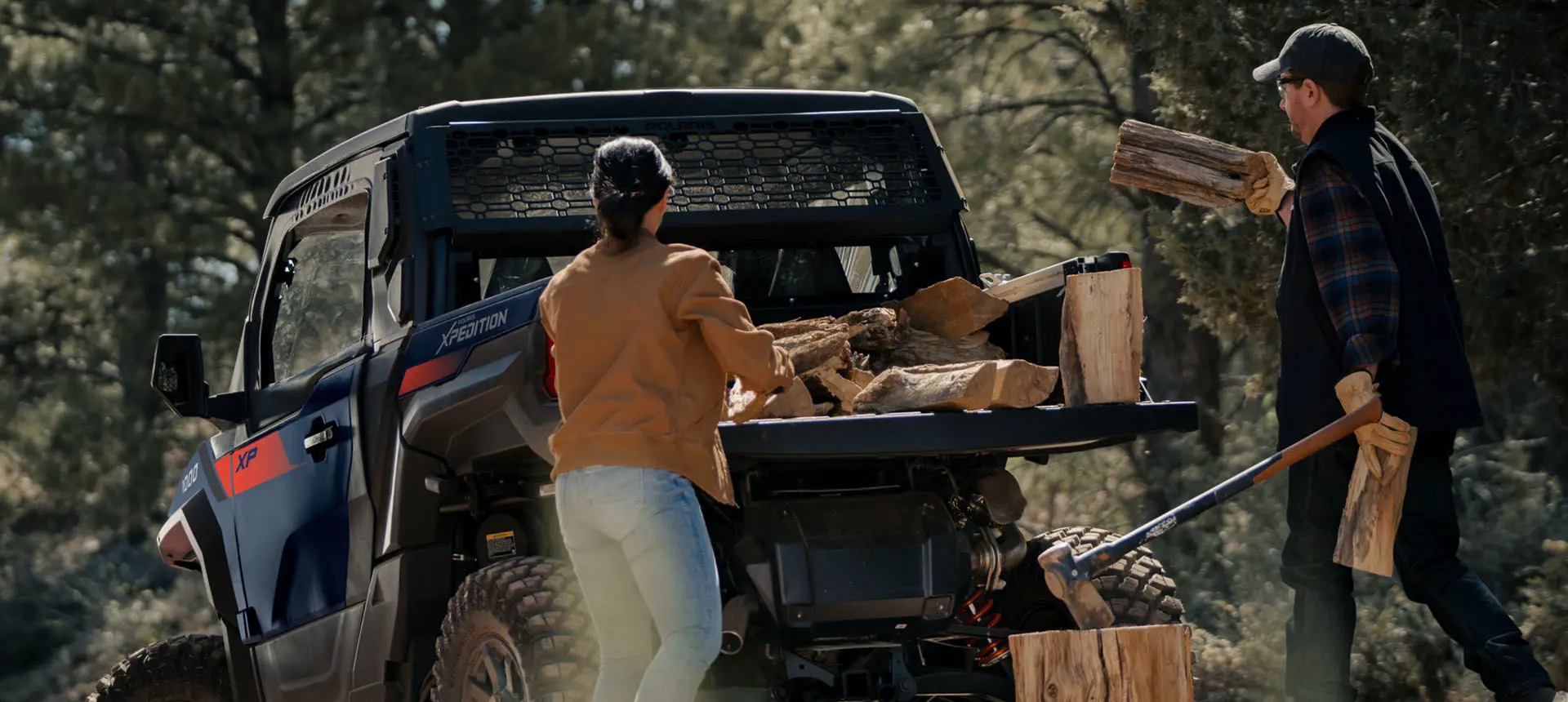People loading firewood into the cargo box of a Polaris XPEDITION XP side-by-side.