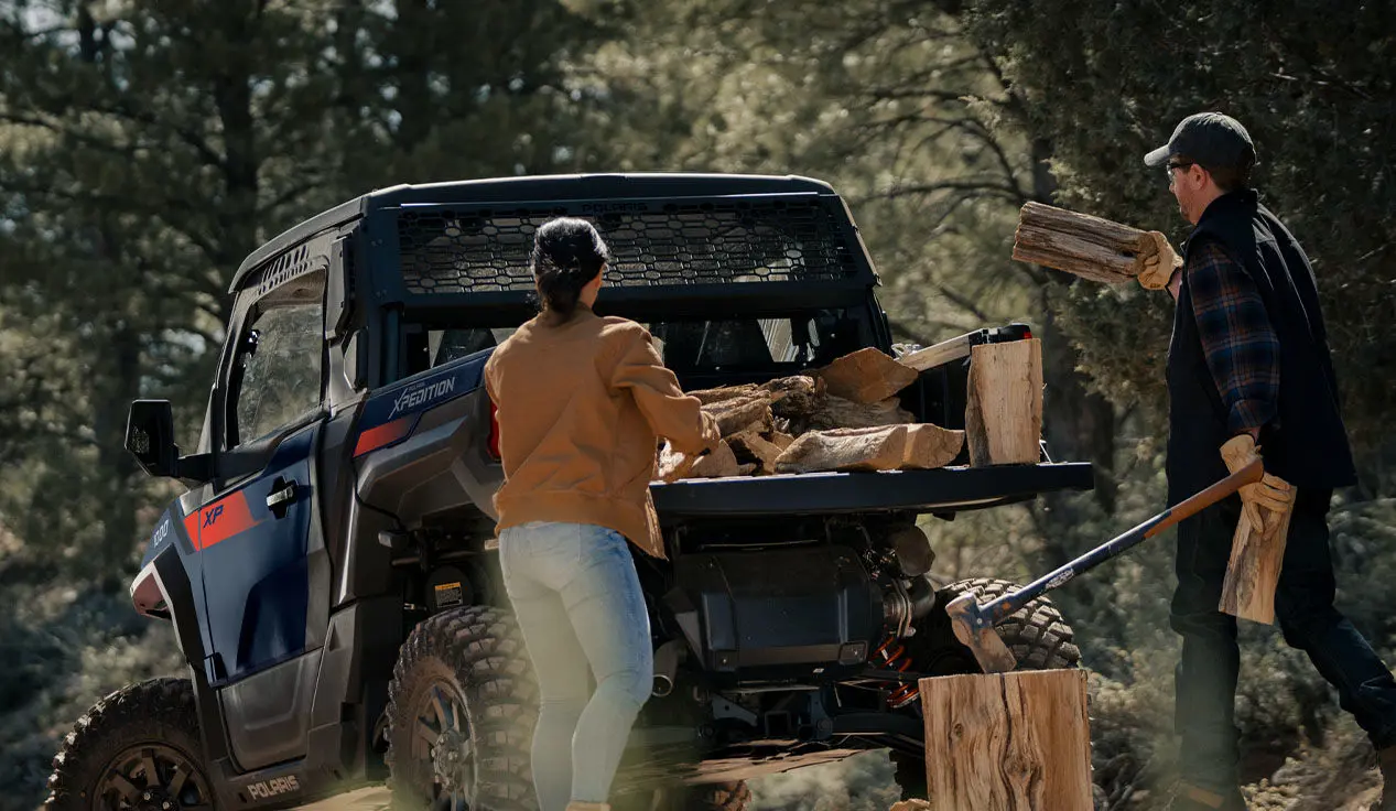 People loading firewood into the cargo box of a Polaris XPEDITION XP side-by-side.