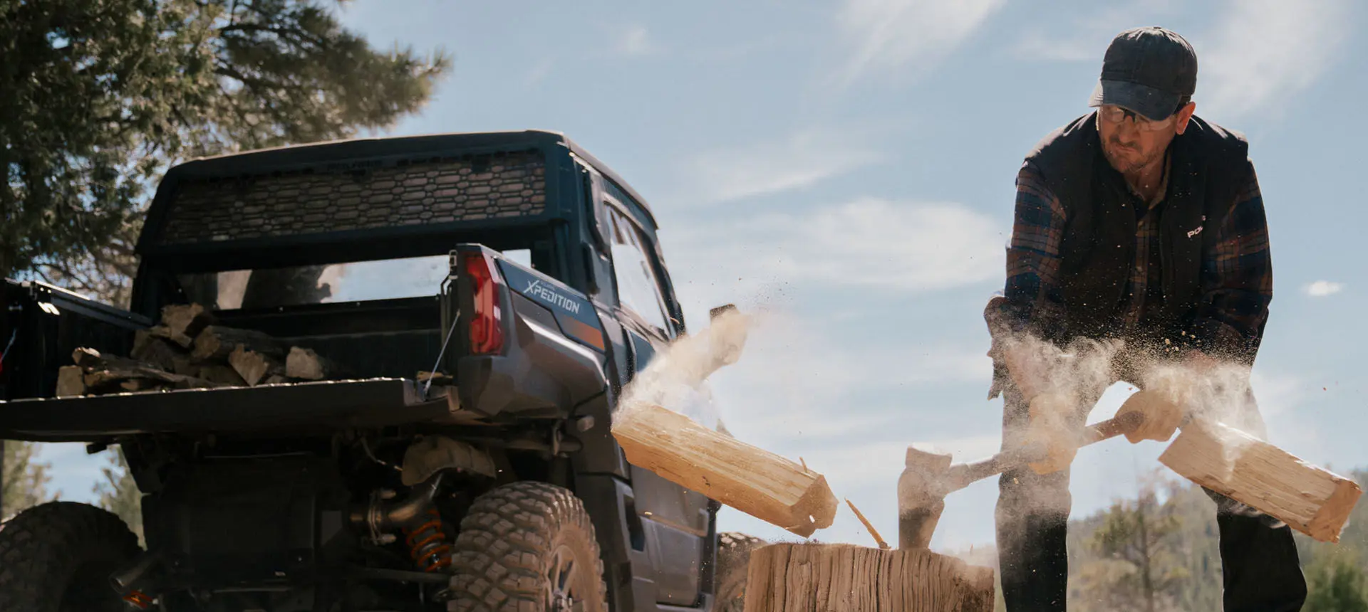 Person splitting wood next to their Polaris XPEDITION XP side-by-side.