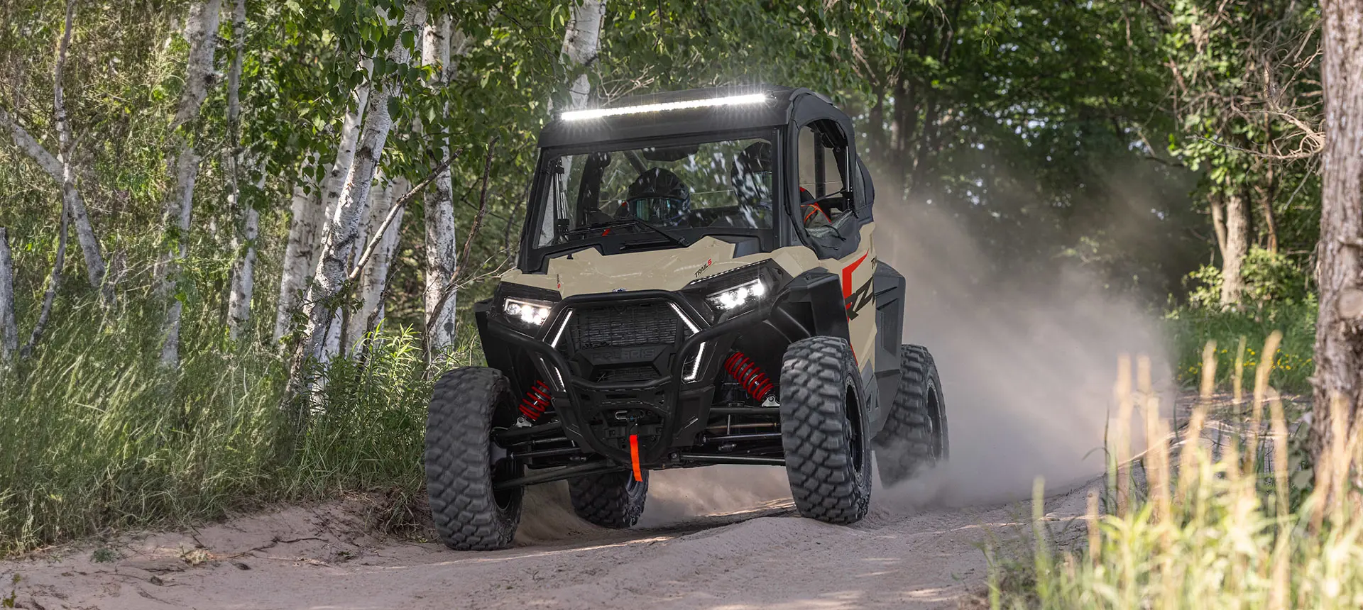 Polaris RZR Trail side-by-side with lights illuminated driving on a trail.