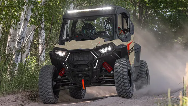 Polaris RZR Trail side-by-side with lights illuminated driving on a trail.