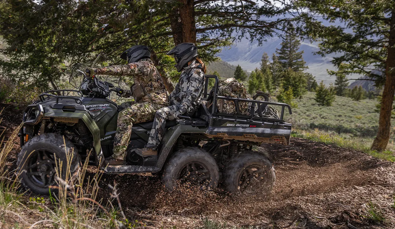 Two hunters riding on a Polaris Sportsman 6x6 570 ATV through mud.