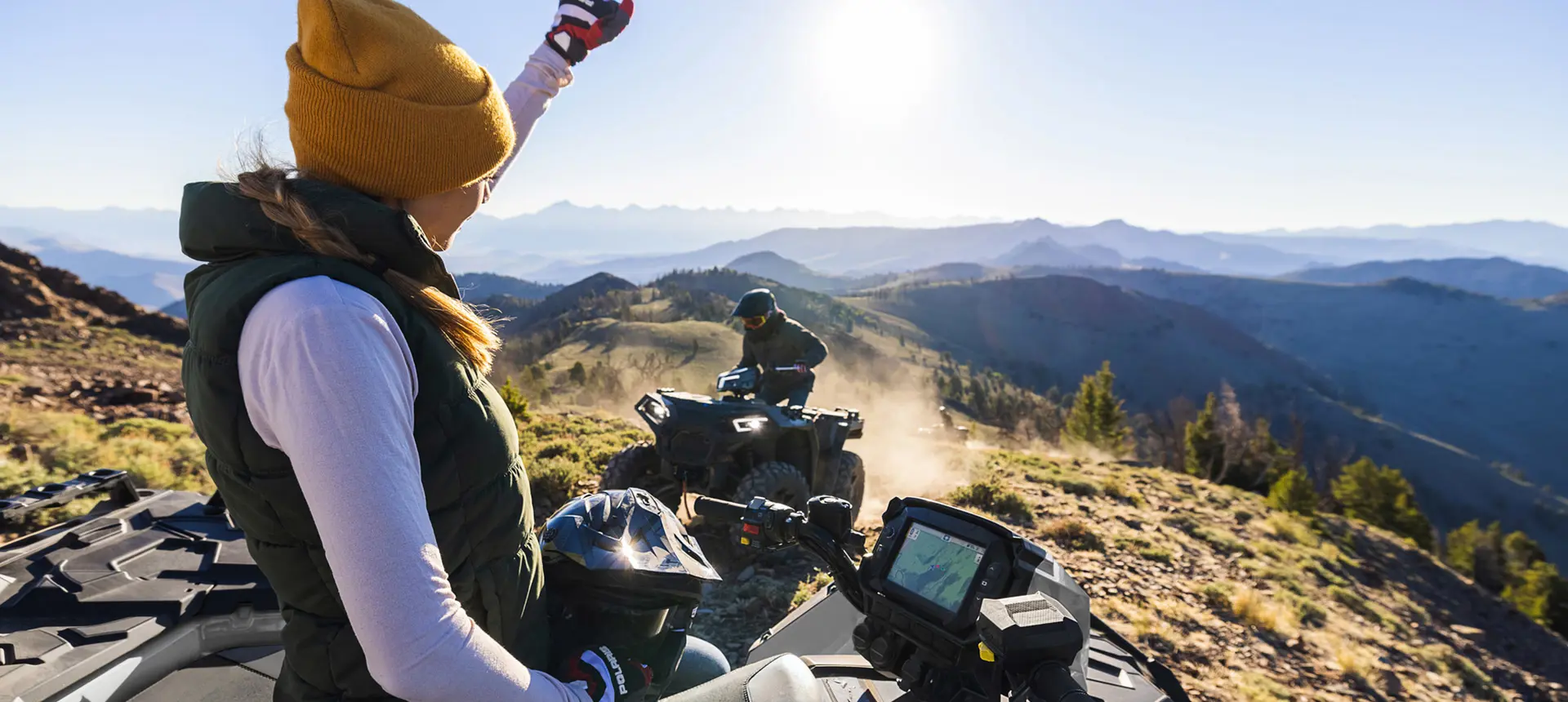 Woman waving to anoter rider on a Polaris Sportsman XP 1000 ATV.
