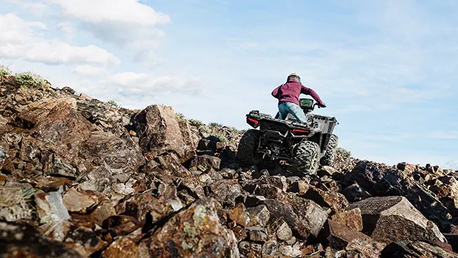 Person climbing rocky terrain with a Polaris Sportsman XP 1000 ATV.