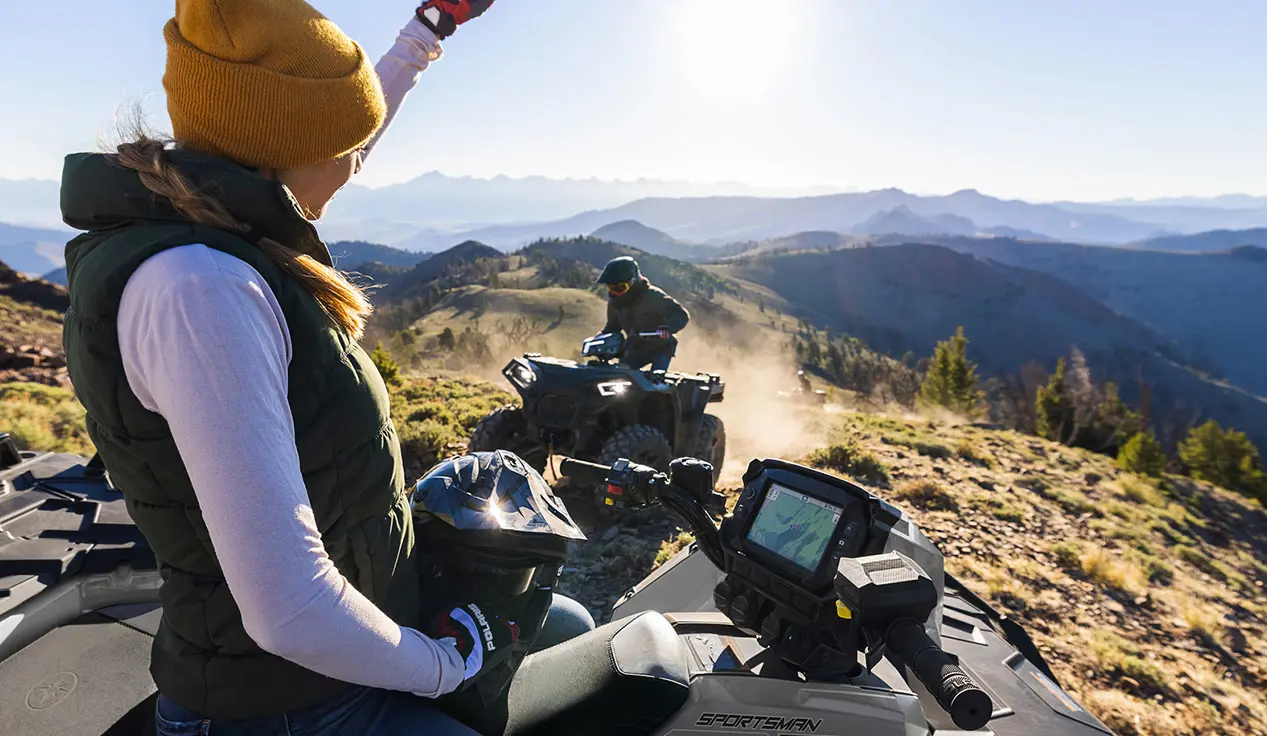 Woman waving to anoter rider on a Polaris Sportsman XP 1000 ATV.