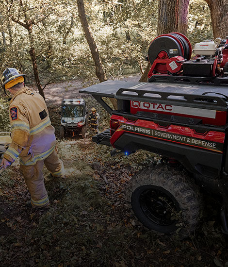 Two firefighters and Polaris Fire & Rescue UTVs with Q-TAC equipment in a wooded area.
