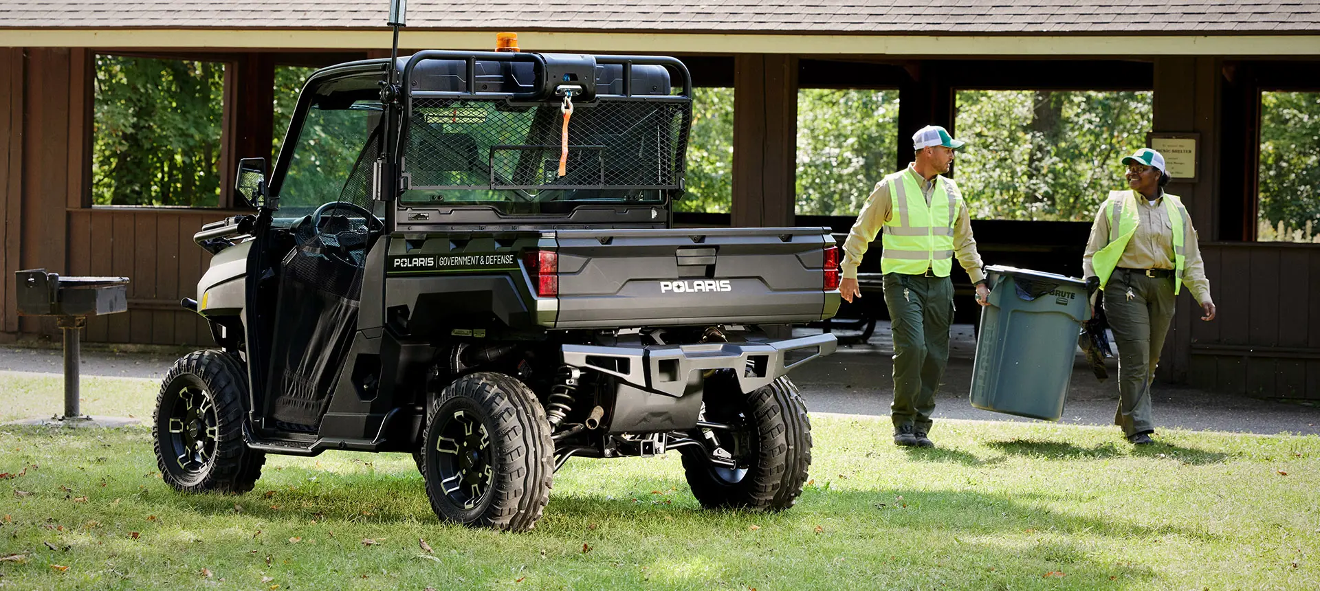 Two workers holding a trash can next to their Polaris RANGER UTV being used for grounds and facility operations.