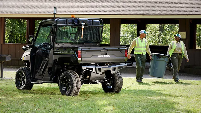 Two workers holding a trash can next to their Polaris RANGER UTV being used for grounds and facility operations.