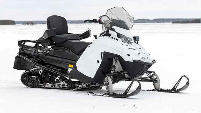 A white and black snowmobile 2026 Military 850 TITAN 155 sits on a snow-covered plain against a distant treeline.