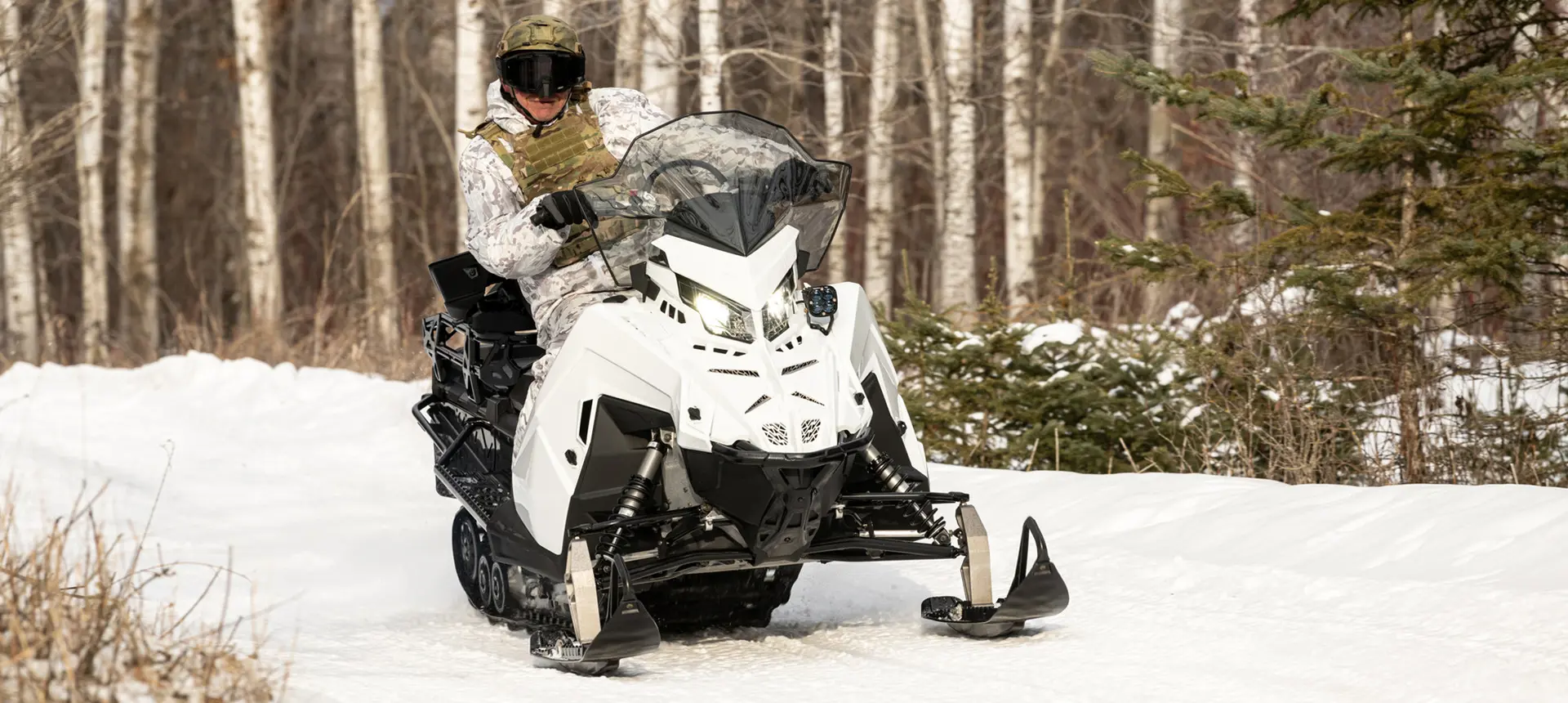 Soldier riding a Polaris Military snowmobile on a trail.