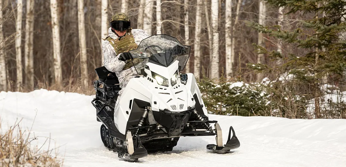 Soldier riding a Polaris Military snowmobile on a trail.