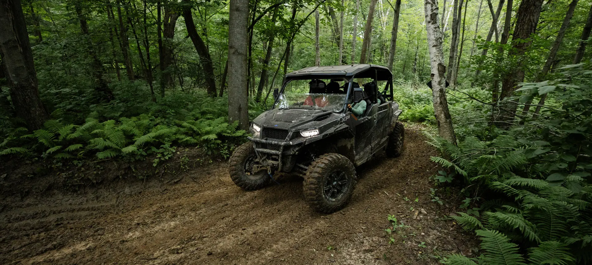 Polaris GENERAL XP 4 1000 side-by-side driving through the forest with a fully loaded cab.