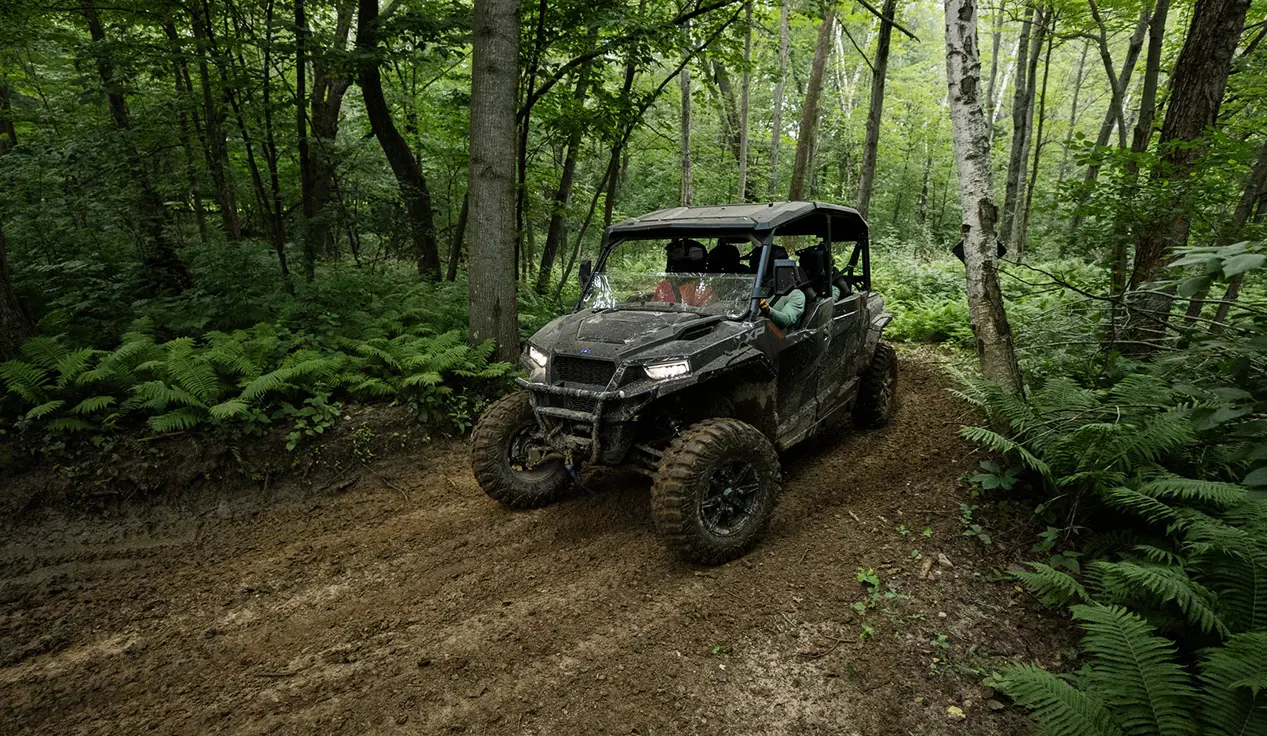 Polaris GENERAL XP 4 1000 side-by-side driving through the forest with a fully loaded cab.