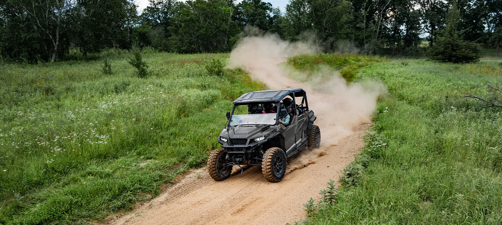 Aerial view of a Polaris GENERAL XP 4 1000 side-by-side driving down a dusty trail with 4 riders.