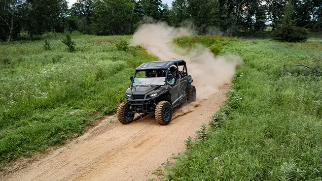 Aerial view of a Polaris GENERAL XP 4 1000 side-by-side driving down a dusty trail with 4 riders.
