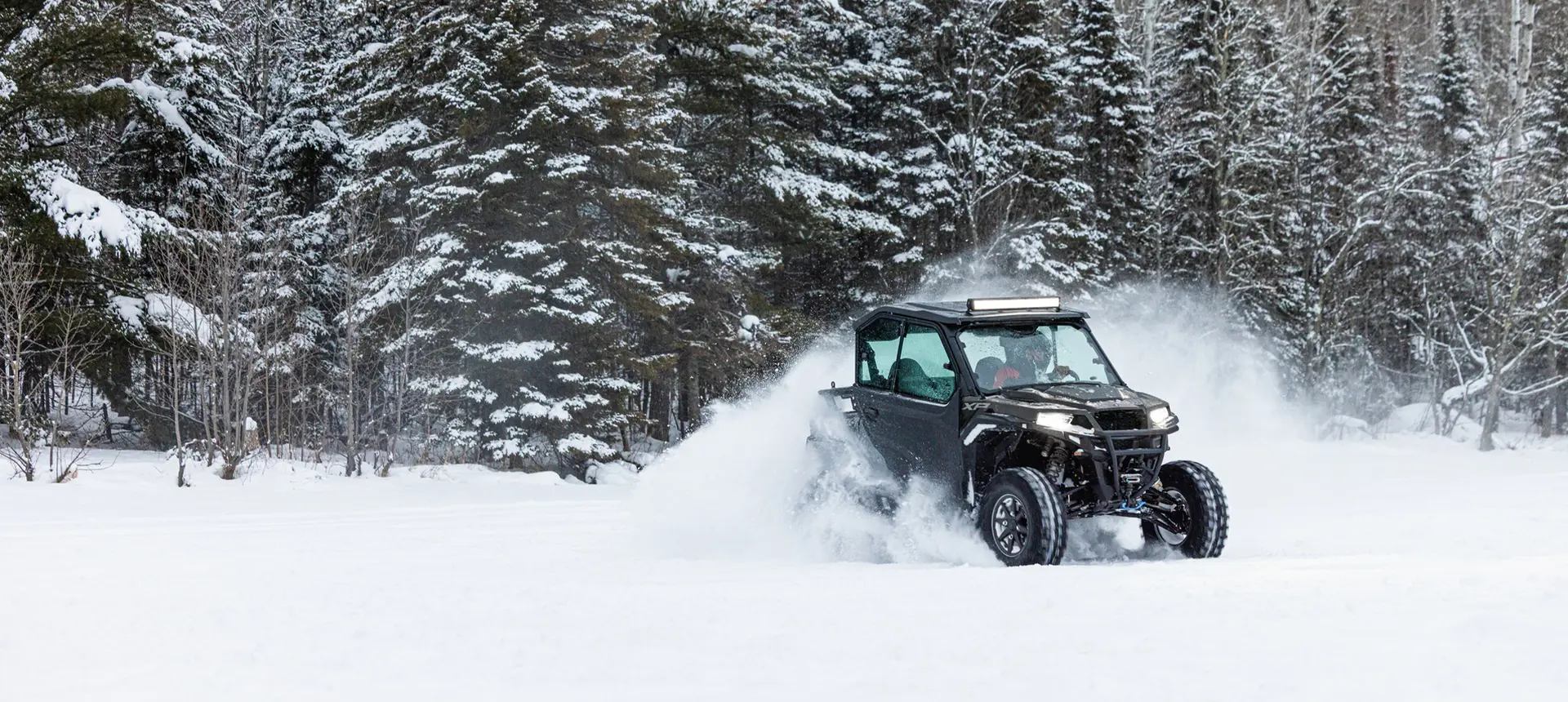 A Polaris GENERAL XP 1000 side-by-side with lightbar and full door accessories installed driving through a snowy field.