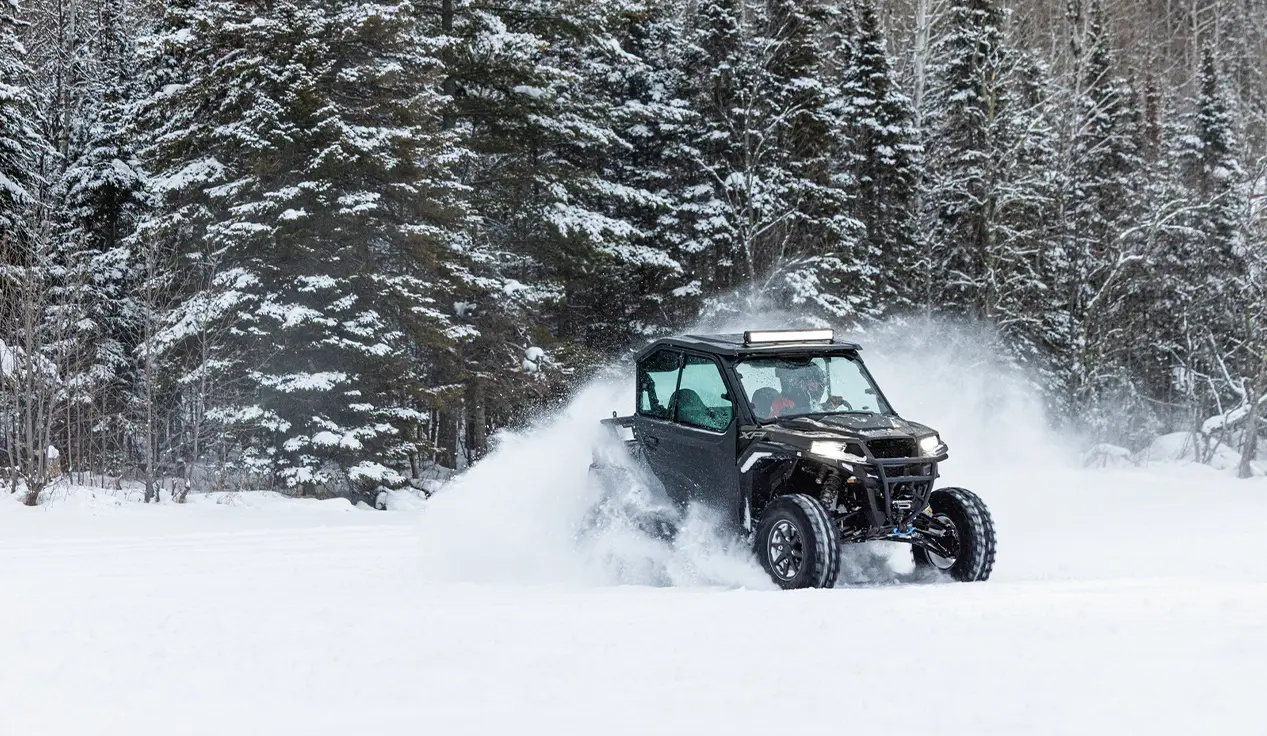 A Polaris GENERAL XP 1000 side-by-side with lightbar and full door accessories installed driving through a snowy field.