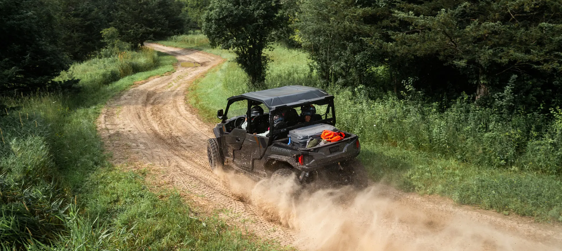 Aerial rear view of a Polaris GENERAL XP 4 1000 side-by-side driving on a dusty trail with 4 riders.