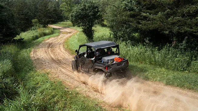 Aerial rear view of a Polaris GENERAL XP 4 1000 side-by-side driving on a dusty trail with 4 riders.