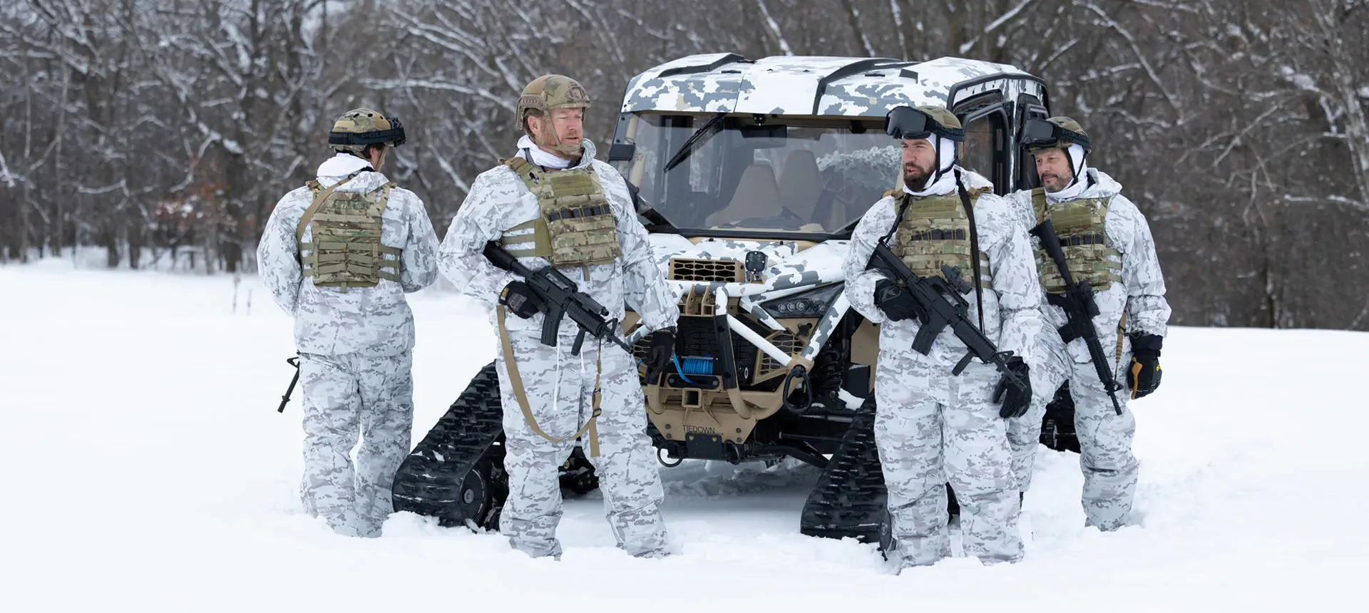 4 soldiers in winter garb standing near a MRZR Alpha military tactical side-by-side with tracks installed.