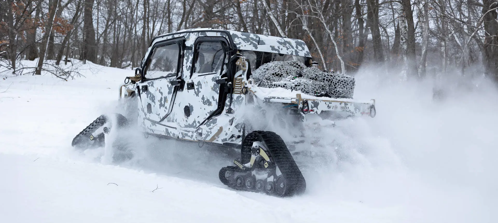Side profile of a MRZR Alpha XP military tactical side-by-side with tracks installed driving on a snowy trail.