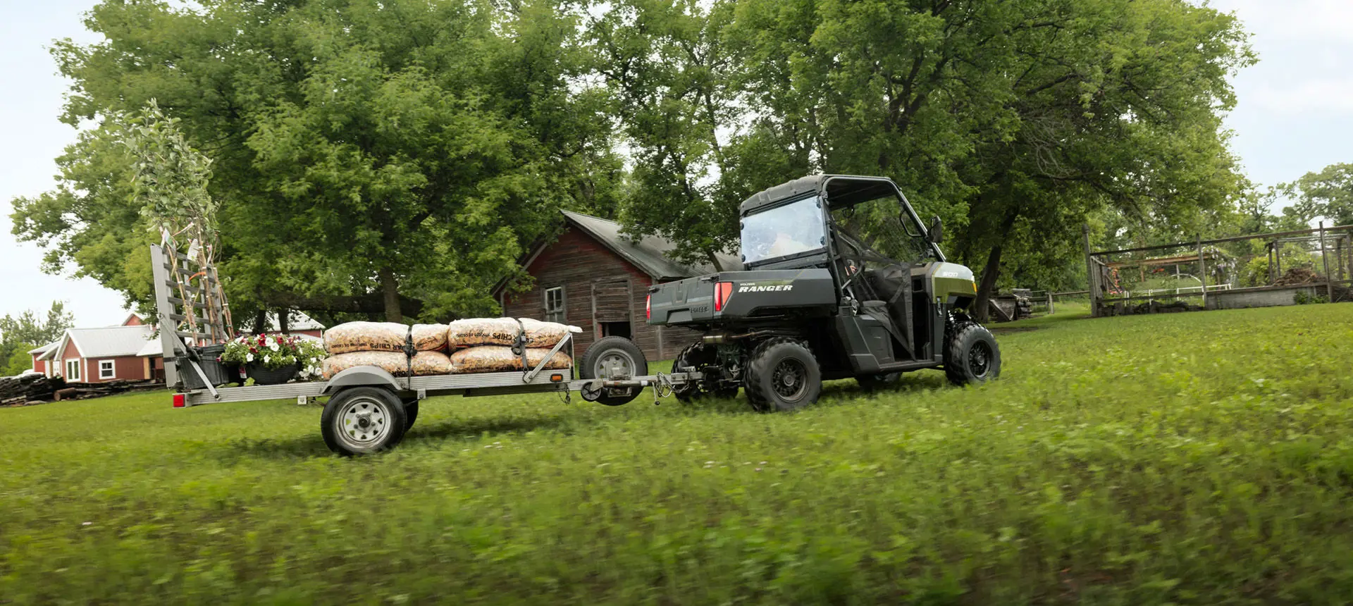 A Sage Green Polaris RANGER 500 UTV pulling a trailer loaded with mulch.