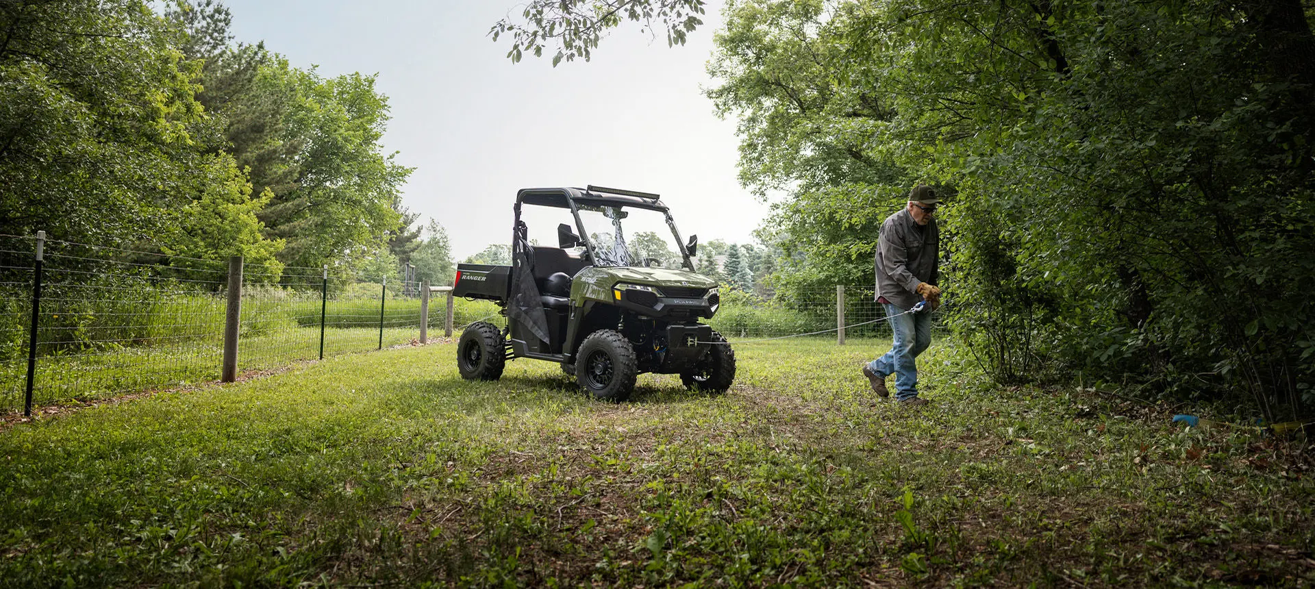 A man pulling out the winch from the front end of a Sage Green Polaris RANGER 500 UTV.