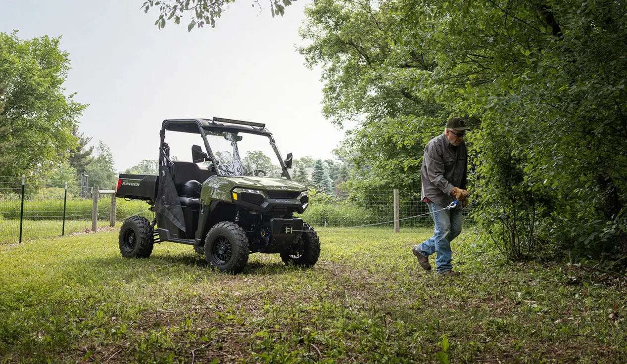 A man pulling out the winch from the front end of a Sage Green Polaris RANGER 500 UTV.