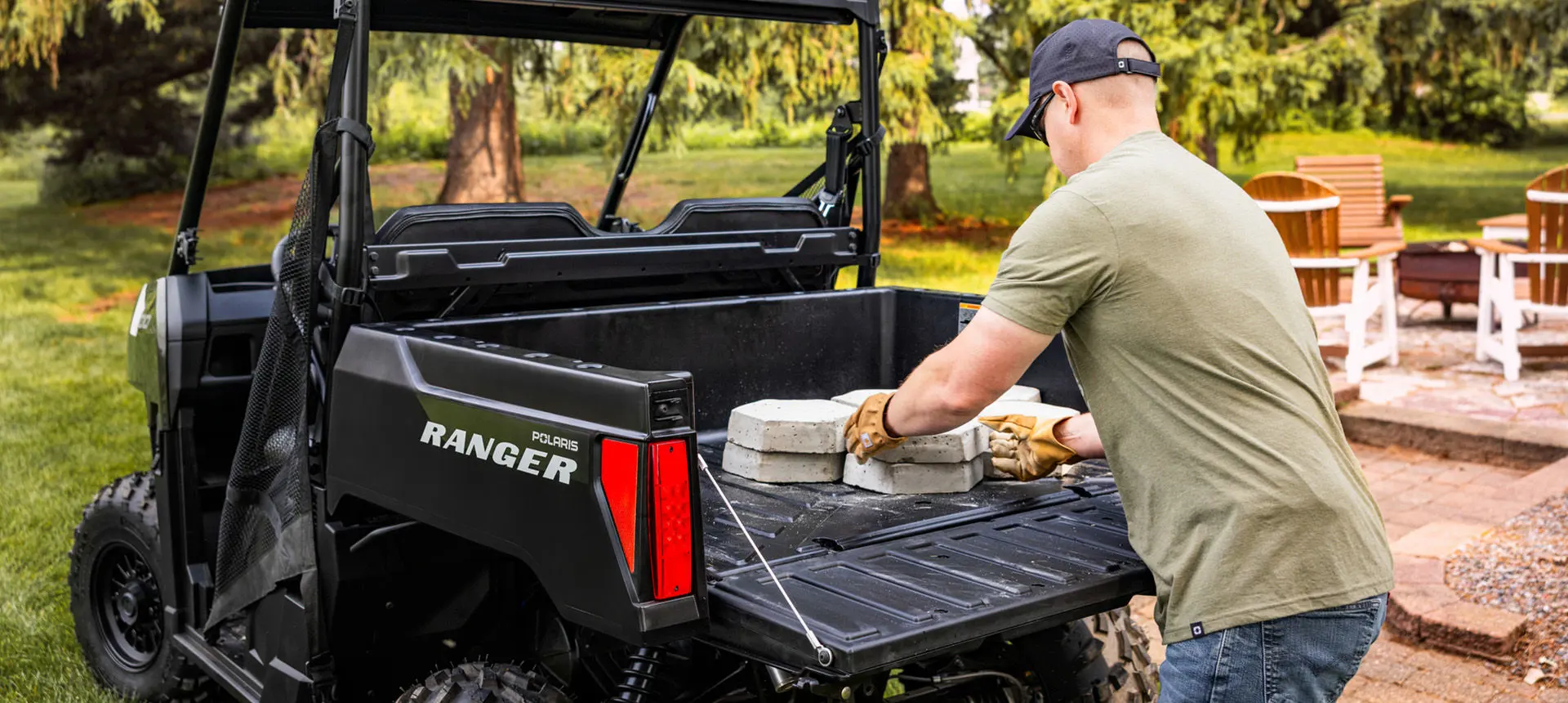 A man loading pavers into the cargo box of a Sage Green Polaris RANGER 500 UTV.