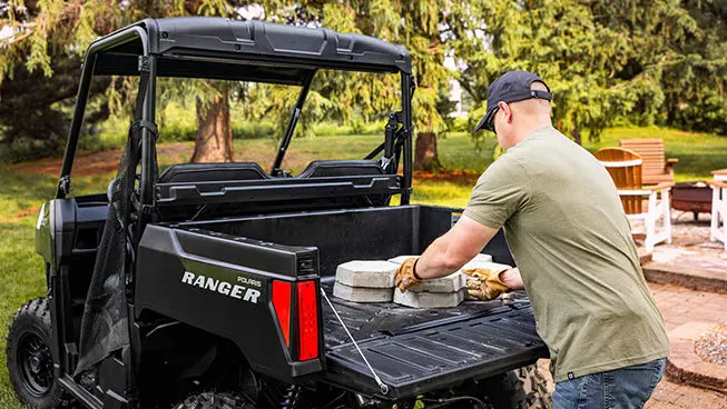 A man loading pavers into the cargo box of a Sage Green Polaris RANGER 500 UTV.