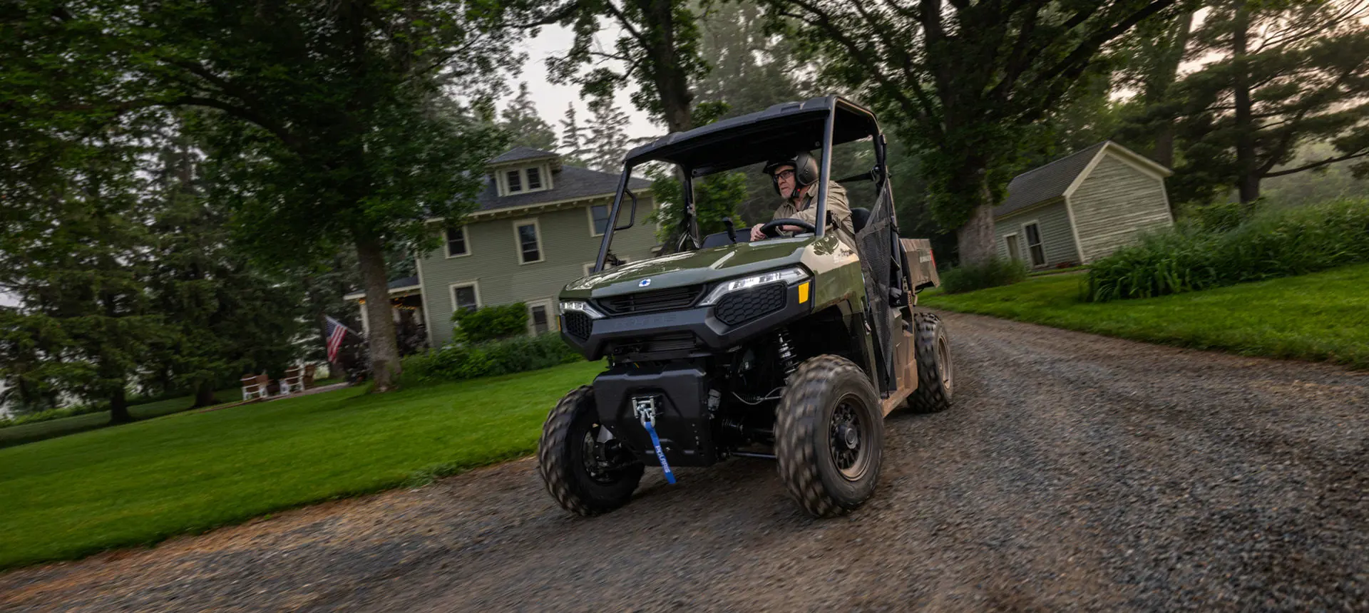 A man driving a Sage Green Polaris RANGER 500 UTV on his driveway.