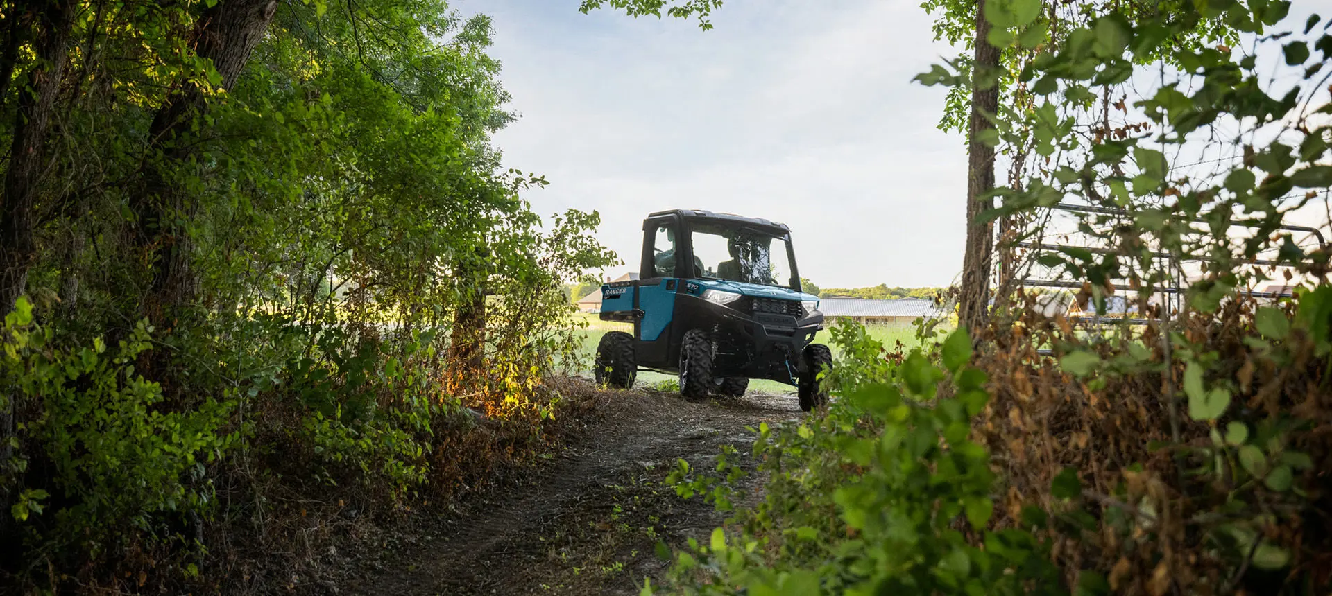 A Polaris RANGER SP 570 NorthStar Edition UTV with illuminated headlights approaching a forest trail.