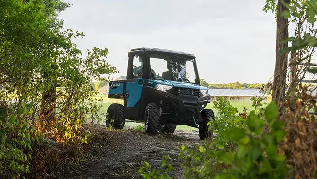 A Polaris RANGER SP 570 NorthStar Edition UTV with illuminated headlights approaching a forest trail.