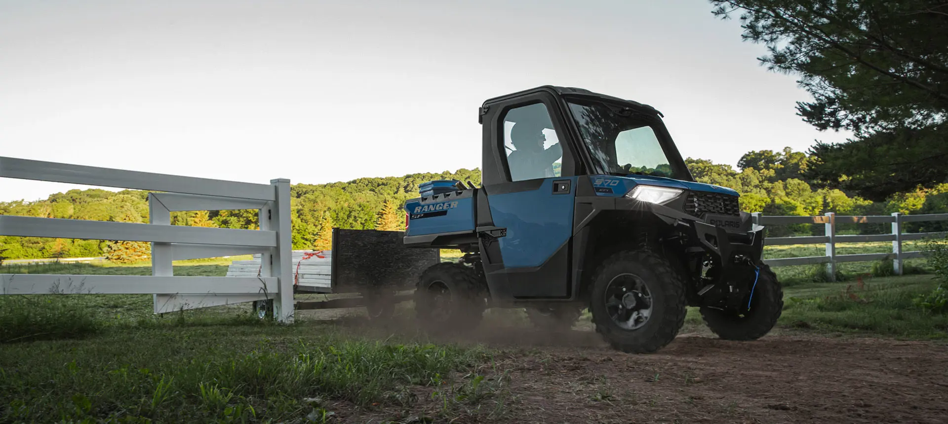 A Polaris RANGER SP 570 NorthStar Edition UTV driving out of a pasture past a gate and fence.