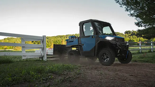 A Polaris RANGER SP 570 NorthStar Edition UTV driving out of a pasture past a gate and fence.