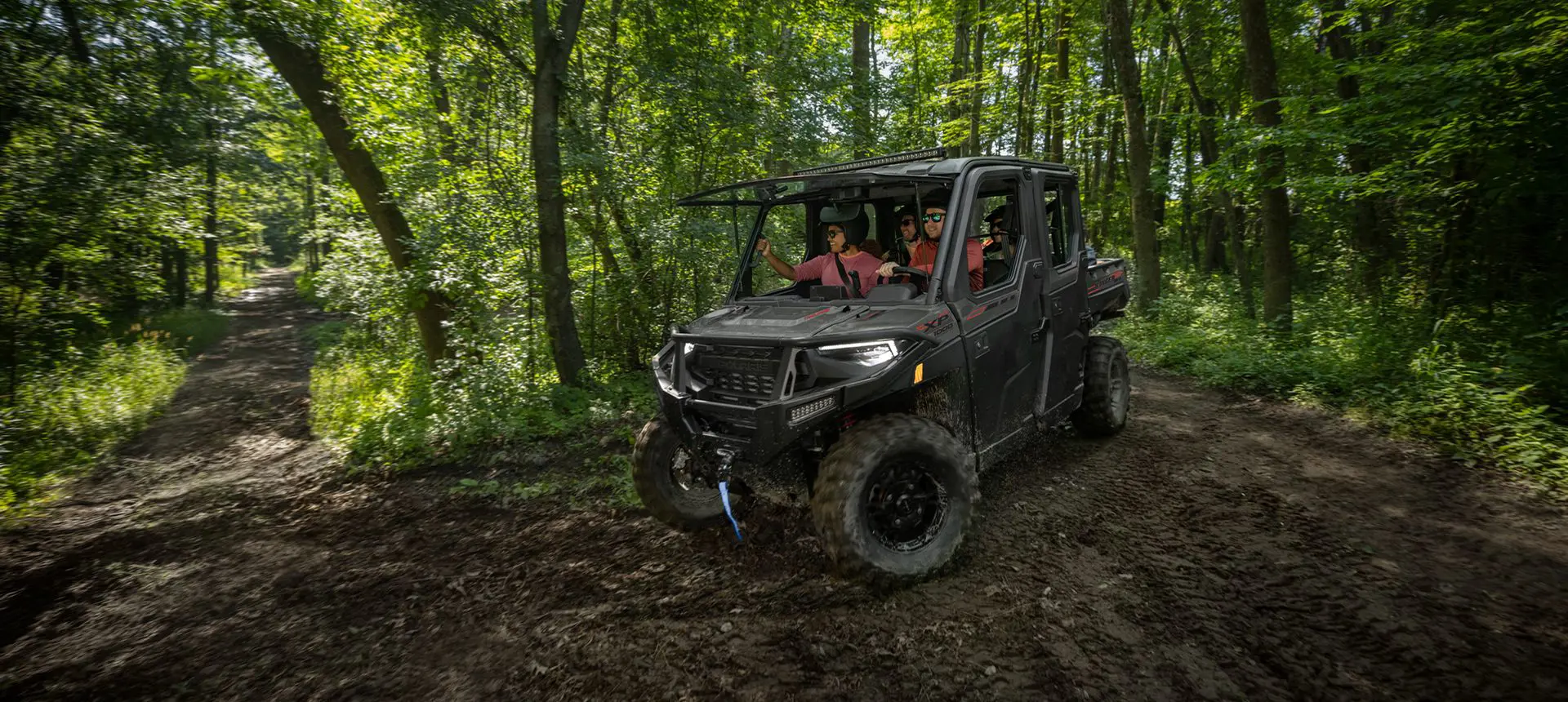 4 riders in a Polaris RANGER CREW XP 1000 NorthStar Edition UTV driving on a forest trail with the windshield tipped out.
