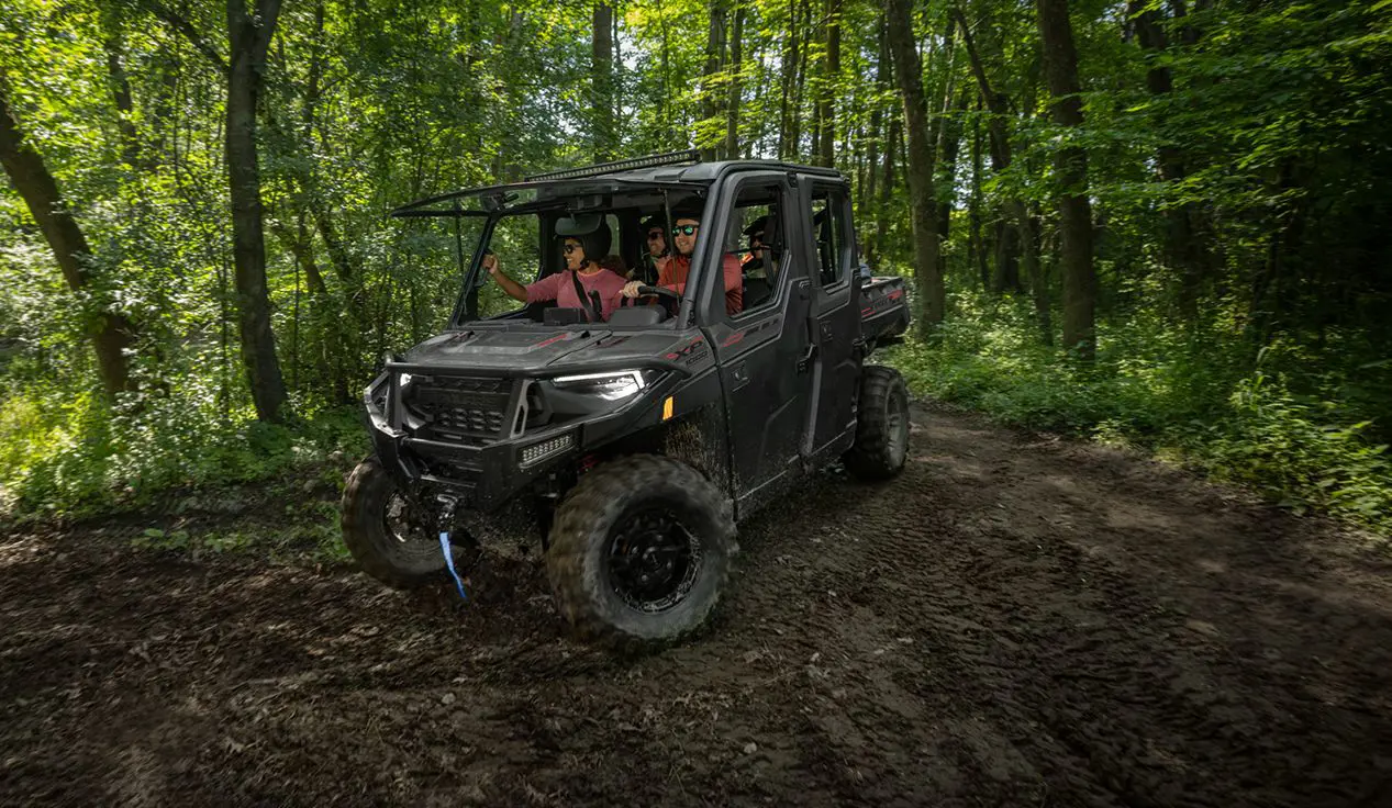 4 riders in a Polaris RANGER CREW XP 1000 NorthStar Edition UTV driving on a forest trail with the windshield tipped out.