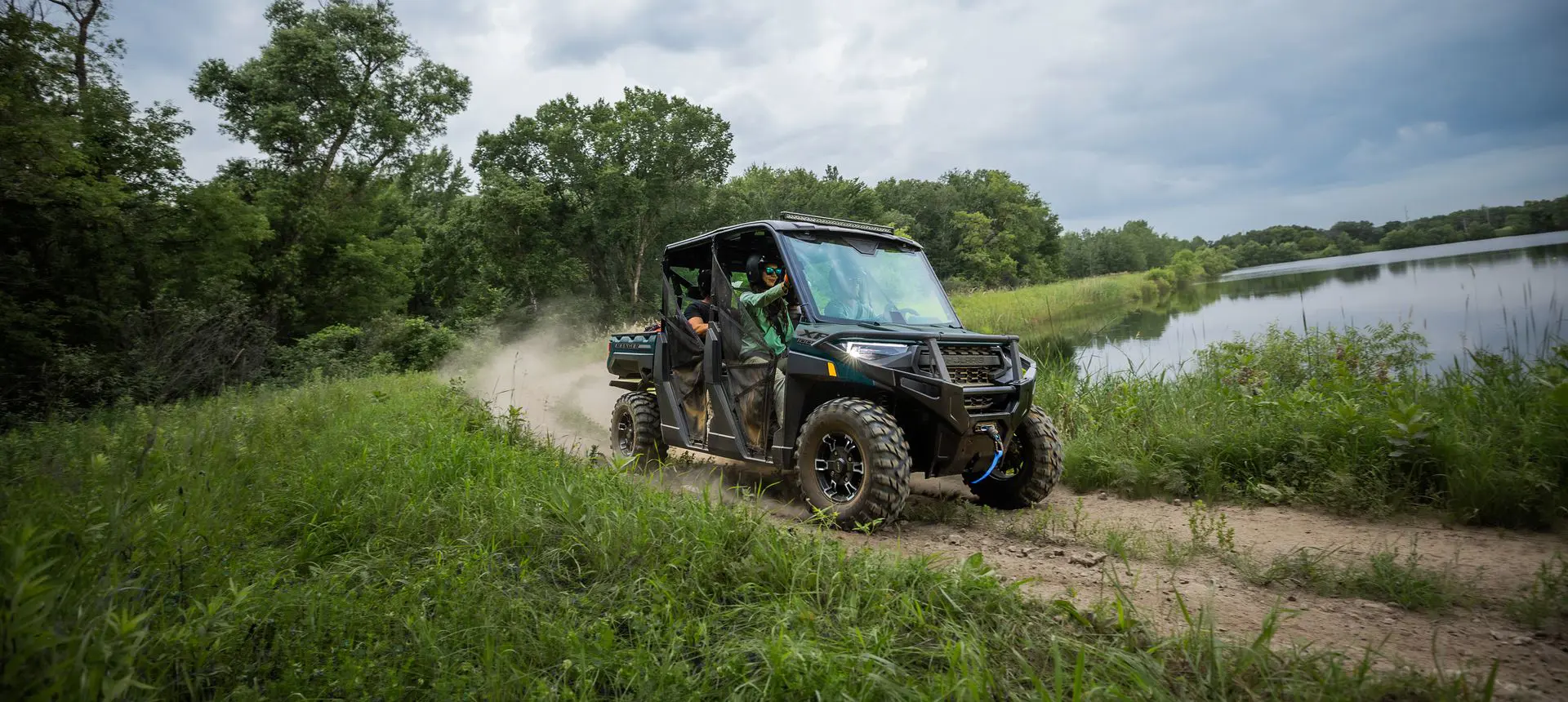 4 riders in a  Polaris RANGER CREW XP 1000 UTV driving on a trail near a lake.