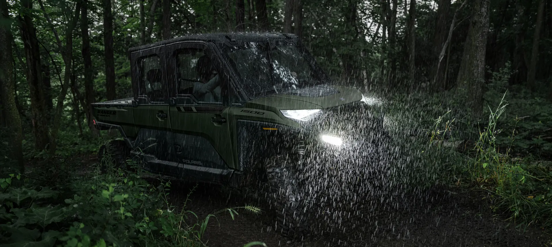 A Polaris RANGER CREW XD 1500 NorthStar Edition extreme duty UTV driving through a forest in the rain.
