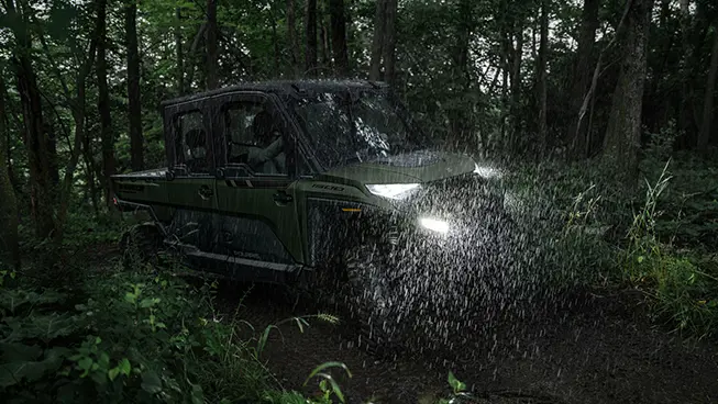 A Polaris RANGER CREW XD 1500 NorthStar Edition extreme duty UTV driving through a forest in the rain.