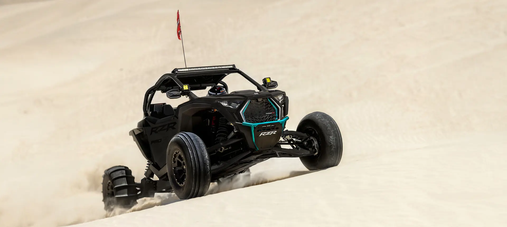A black Polaris RZR Pro R side-by-side crawling up the hills in the dunes.