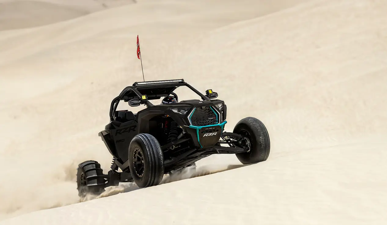 A black Polaris RZR Pro R side-by-side crawling up the hills in the dunes.
